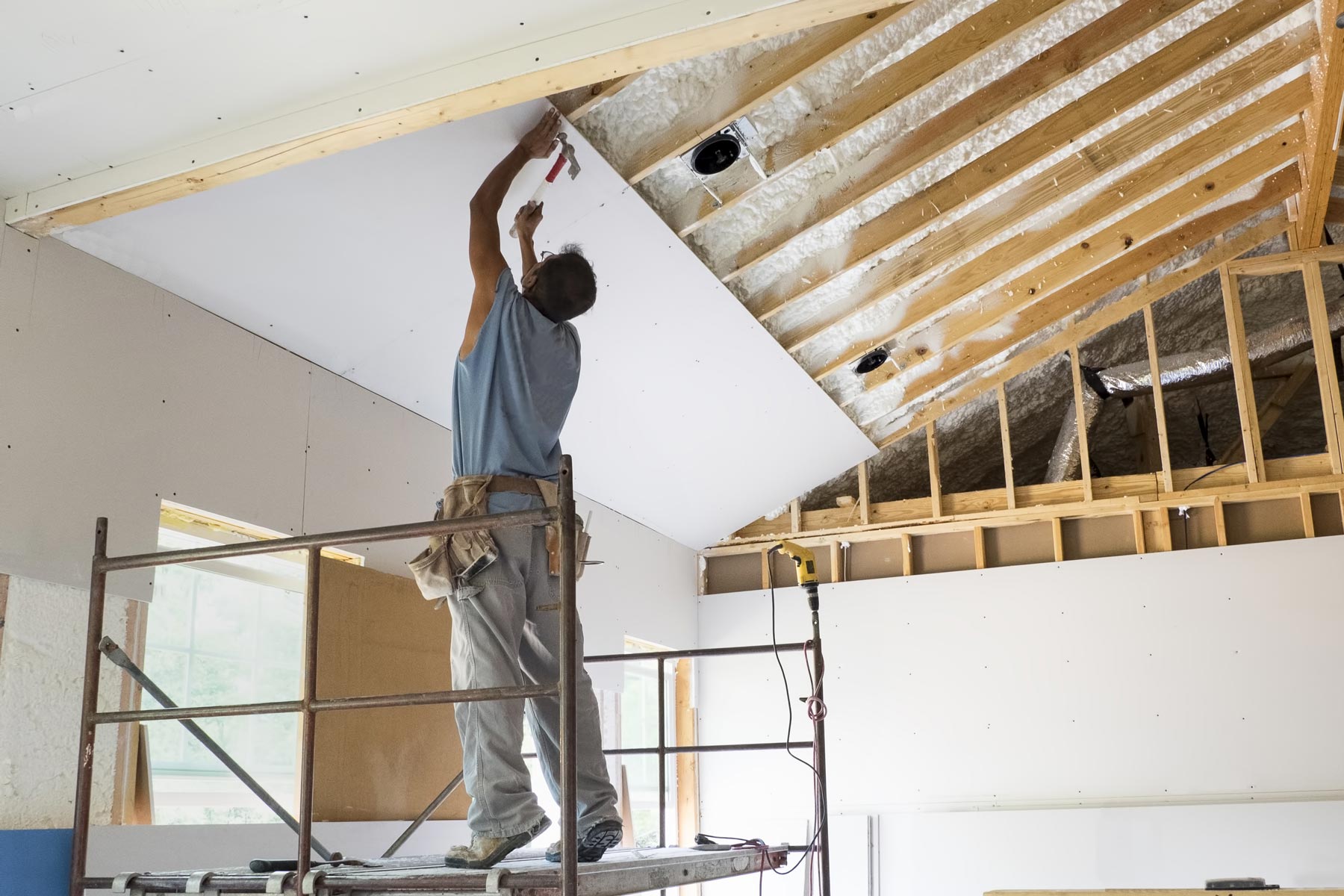 A picture of a man hanging dry wall using a hammer and nails