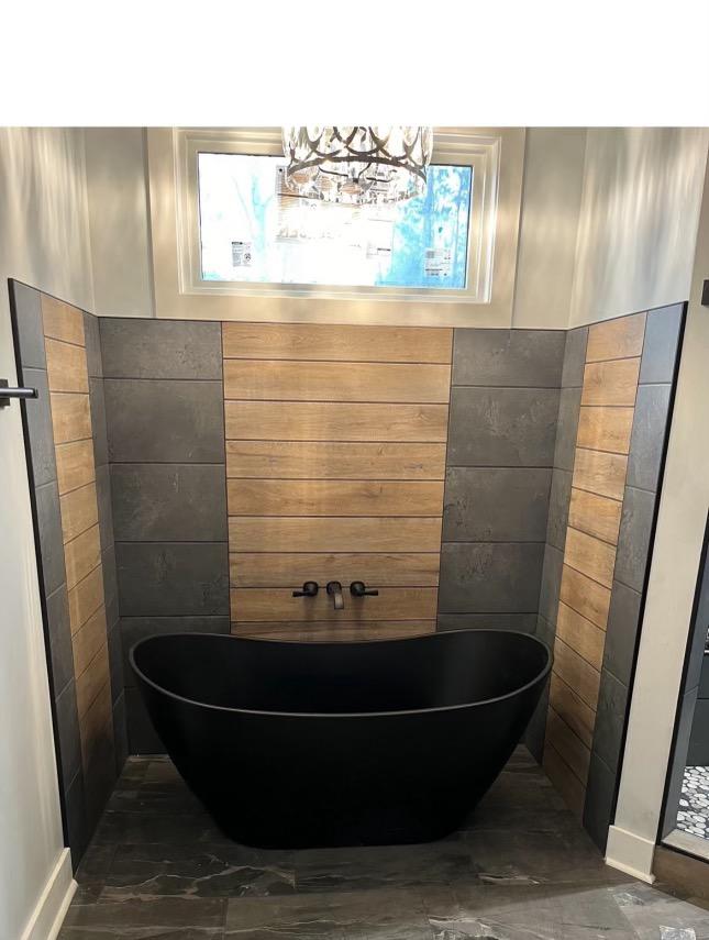 A new bathtub installed and designed for a home. It is black with a wooden accent on the walls